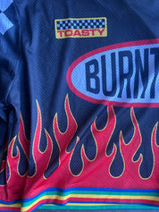 Close-up of a blue mesh jersey with red and pink flame graphics along the bottom, a large oval 'BURNT' logo on the chest, and a 'TOASTY' patch near the shoulder