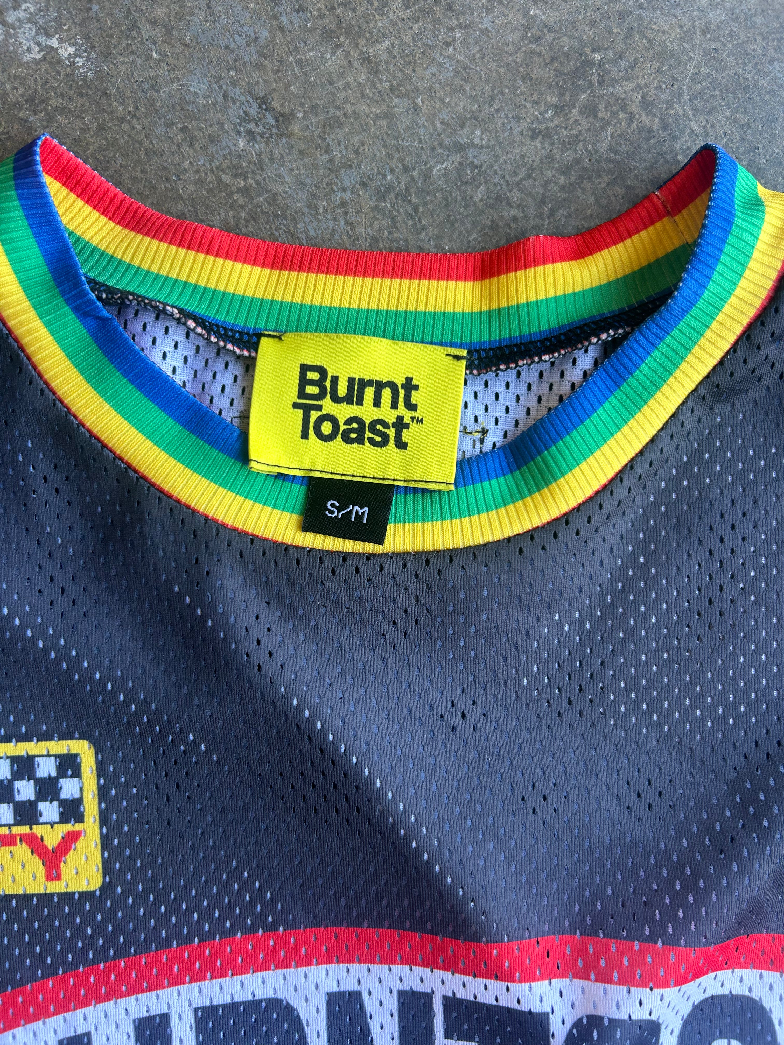 Close-up of a Burnt Toast athletic jersey showing the colorful rainbow collar, yellow brand label, and navy mesh fabric