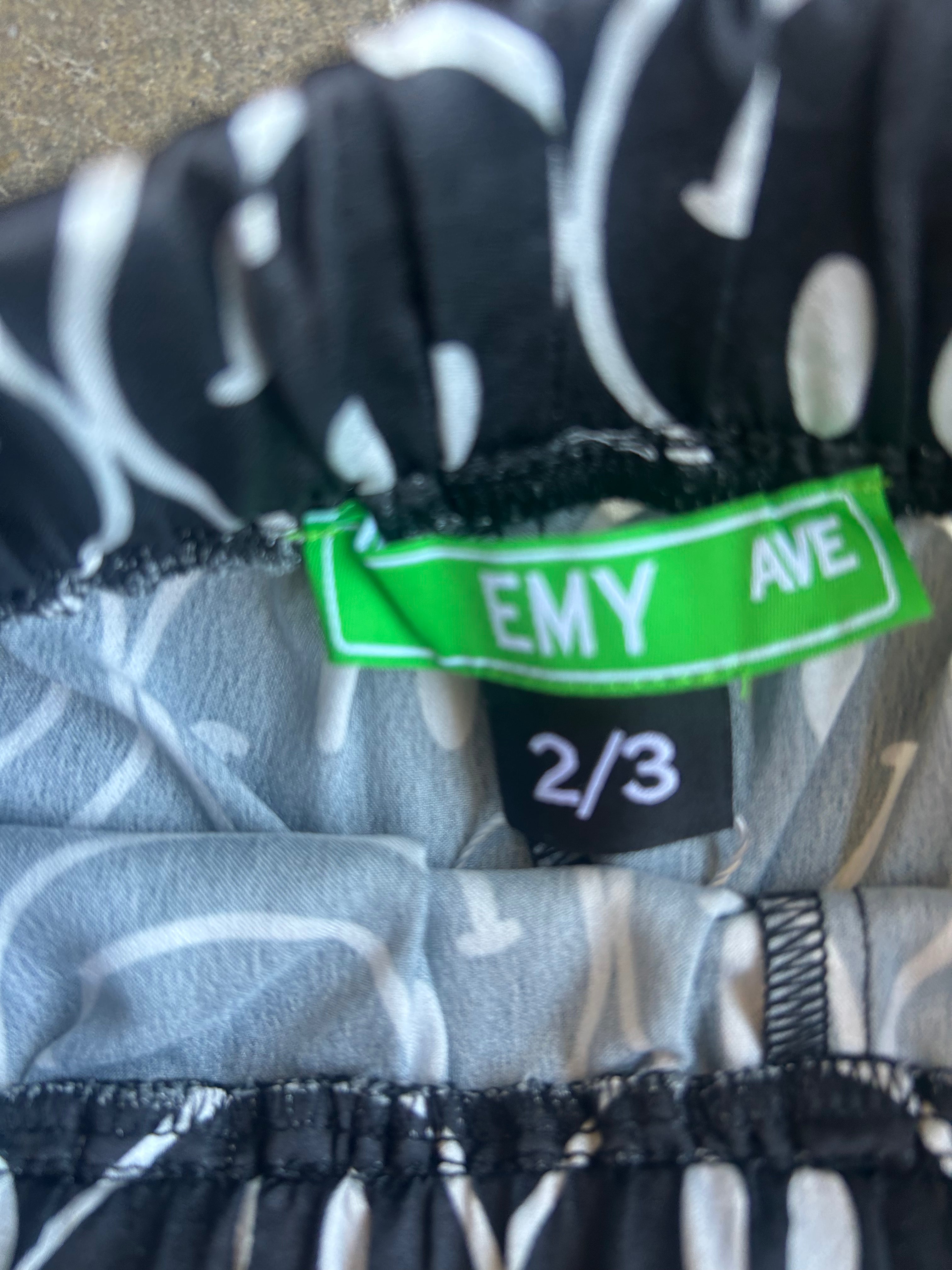 Close-up of a garment's waistband showing a black and white patterned exterior, a light gray interior lining, and two tags: a bright green 'EMY AVE' brand tag and a black size tag reading '2/3'