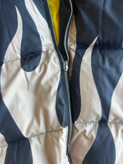 Close-up of a quilted puffer vest with a navy and cream flame-like pattern, featuring a silver zipper and a glimpse of yellow lining