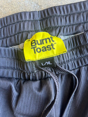 Close-up of dark gray ribbed shorts with an elastic waistband, featuring a bright yellow Burnt Toast brand label and black drawstrings