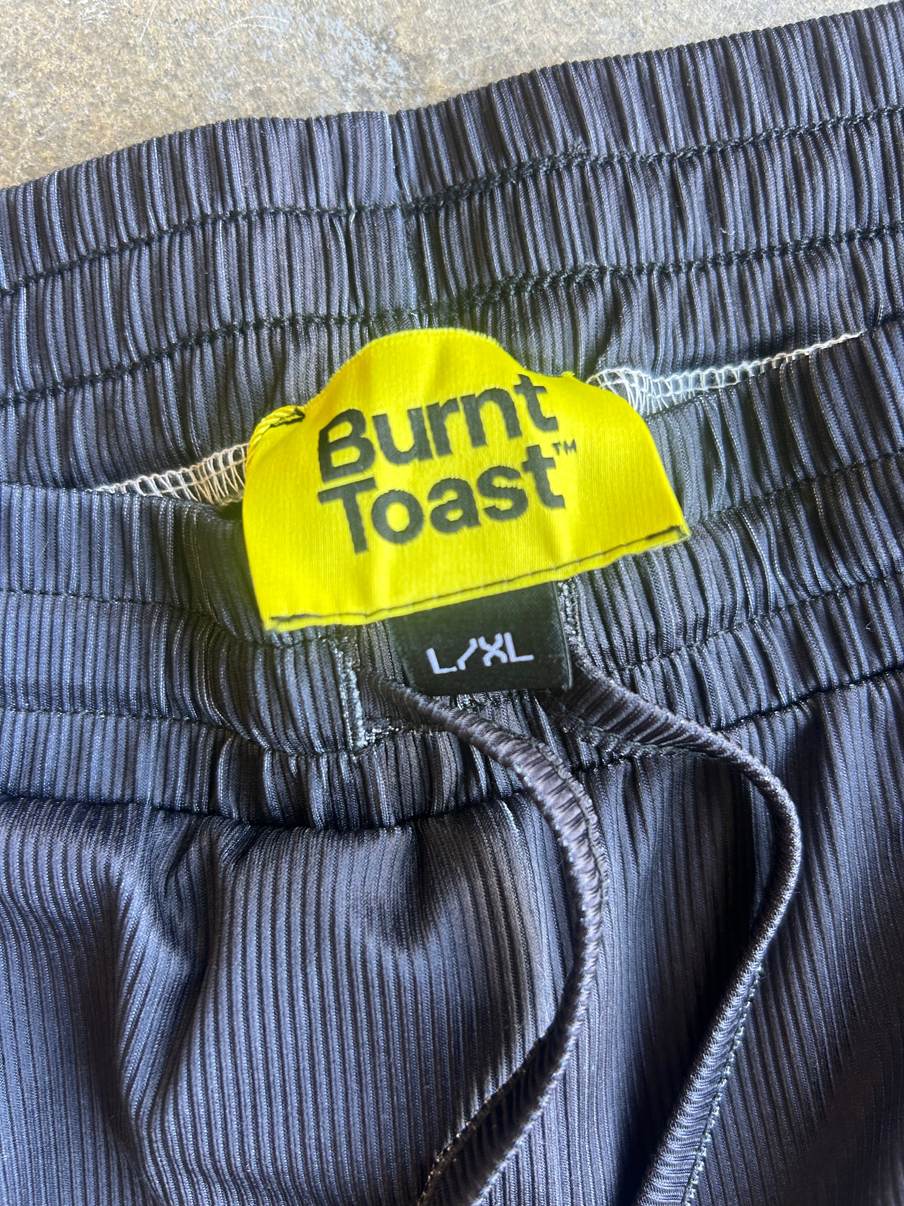 Close-up of dark gray ribbed shorts with an elastic waistband, featuring a bright yellow Burnt Toast brand label and black drawstrings