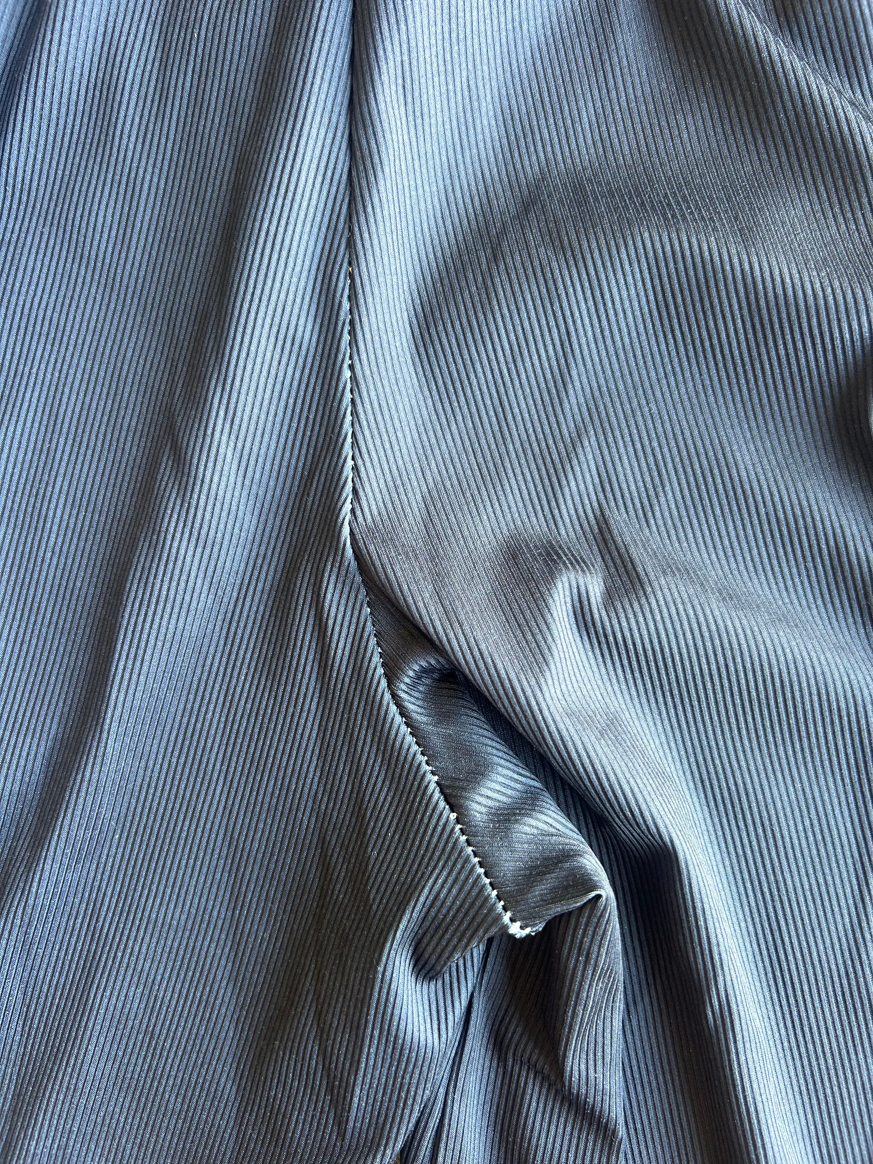 A close-up of draped slate blue corduroy fabric, showing the fine vertical ribbed texture and a neat white zigzag stitch along the edge