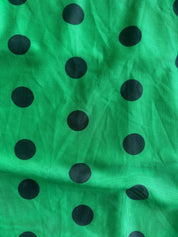 Green fabric with a black polka dot pattern, shown in a close-up view with visible folds and texture