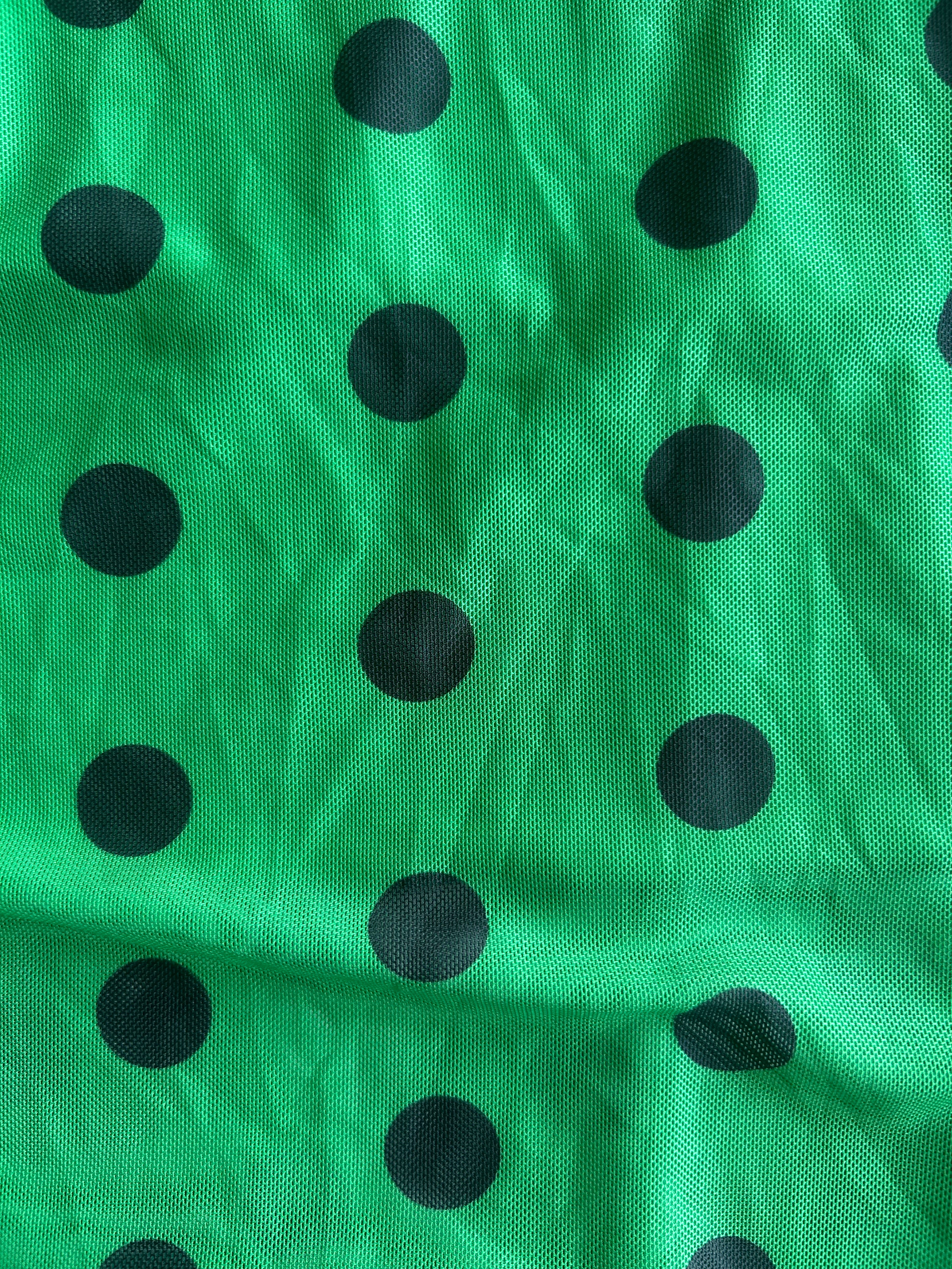 Green fabric with a black polka dot pattern, shown in a close-up view with visible folds and texture