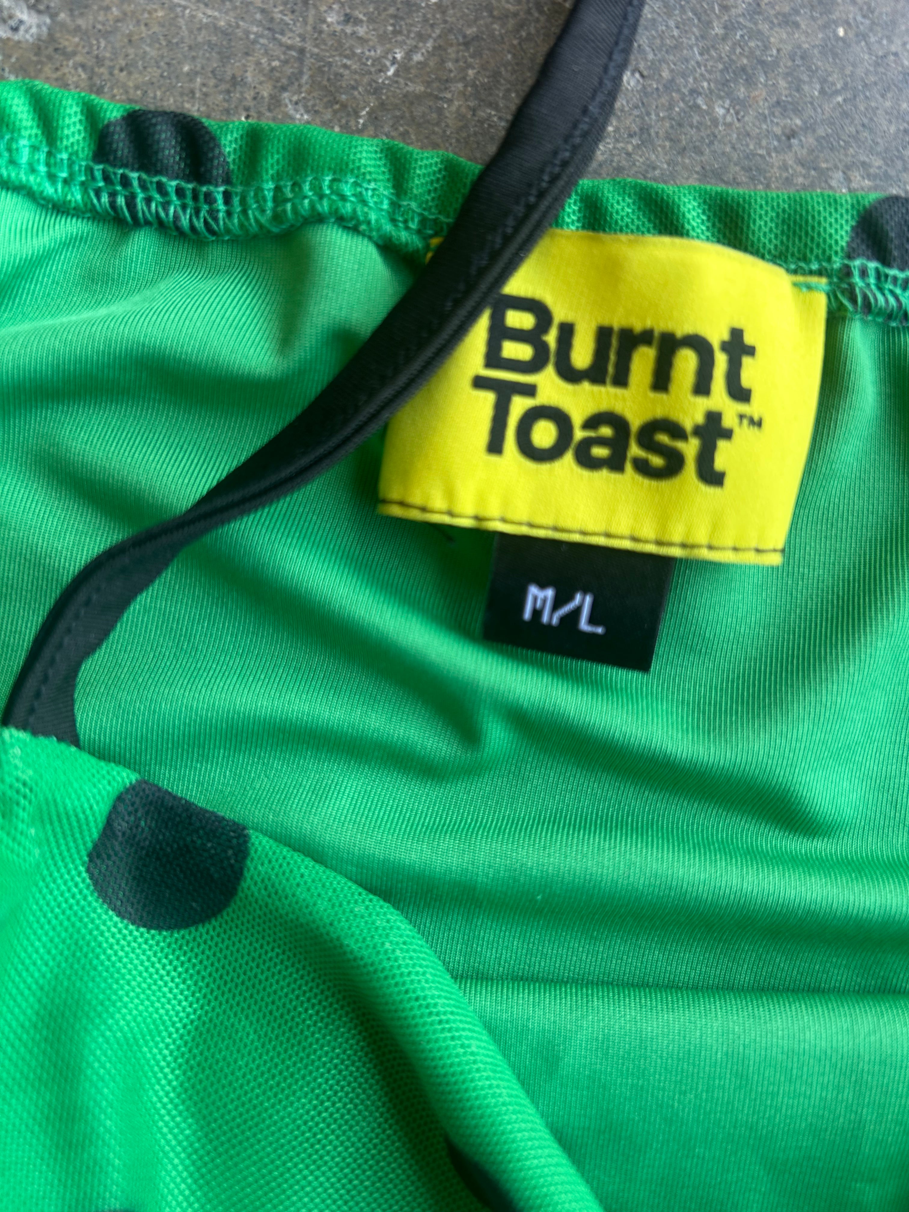 Close-up of a bright green garment with black trim and a yellow Burnt Toast brand label reading M/L