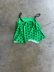 A green short-sleeve top with black polka dots and thin black shoulder straps, laid flat on a textured concrete floor