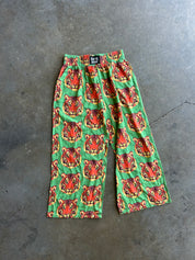 Green wide-leg pants with a repeating red and orange tiger face pattern, laid flat on a gray concrete floor