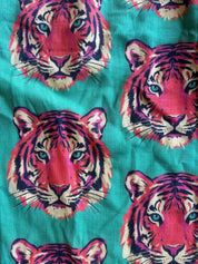 A close-up of fabric featuring a repeating pattern of stylized tiger faces in pink, purple, cream, and black on a bright turquoise background