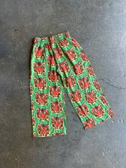 Green pants with a repeating red and orange tiger face pattern, laid flat on a gray concrete floor