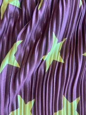 A close-up of pleated fabric in a deep plum purple color, decorated with large lime green star patterns