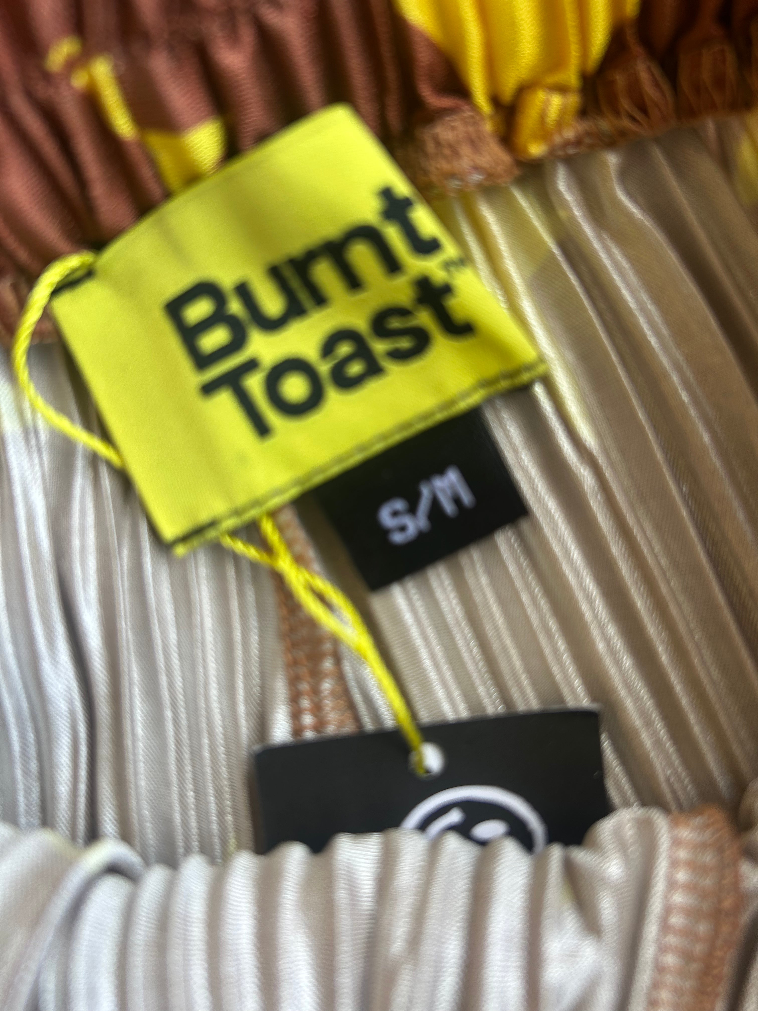 Close-up of a garment tag reading Burnt Toast, with a black S/M size label and another black tag below, on a beige and brown ribbed fabric