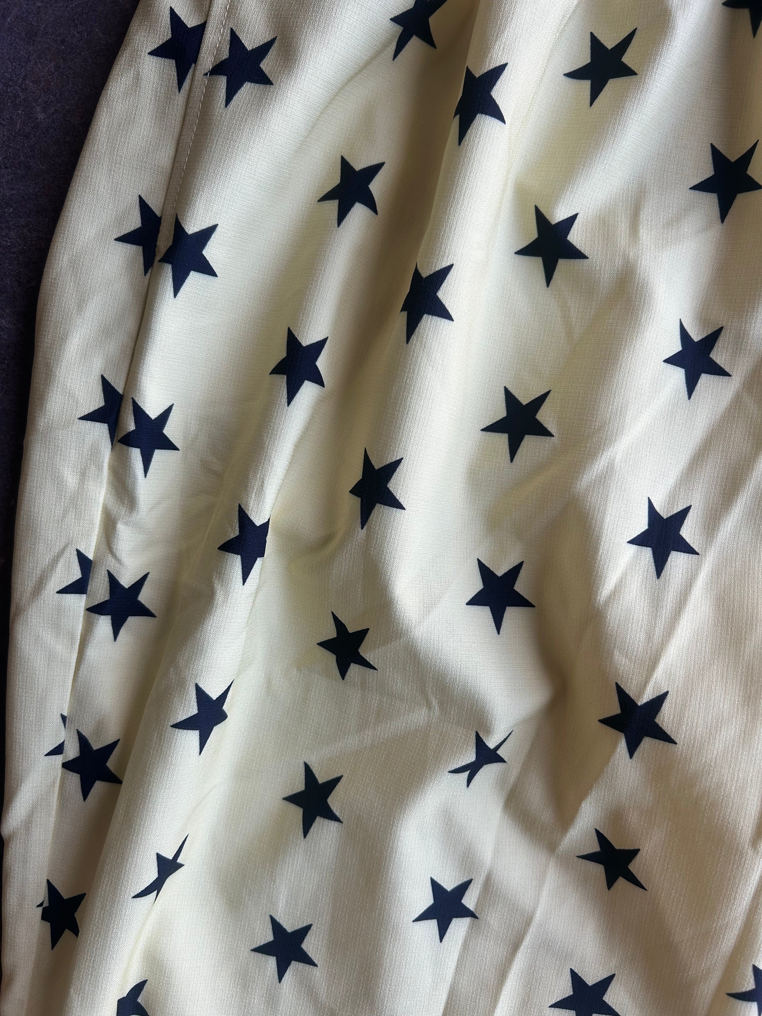 An off-white fabric with a repeating pattern of dark navy blue five-pointed stars, shown with soft folds