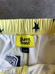 Close-up of the waistband and interior label of Burnt Toast shorts, showing a yellow elastic waist with black star print, a yellow brand label, and a hangtag