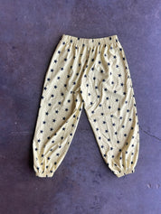 A pair of beige or cream-colored pants with an all-over navy blue star pattern, laid flat on a dark textured surface