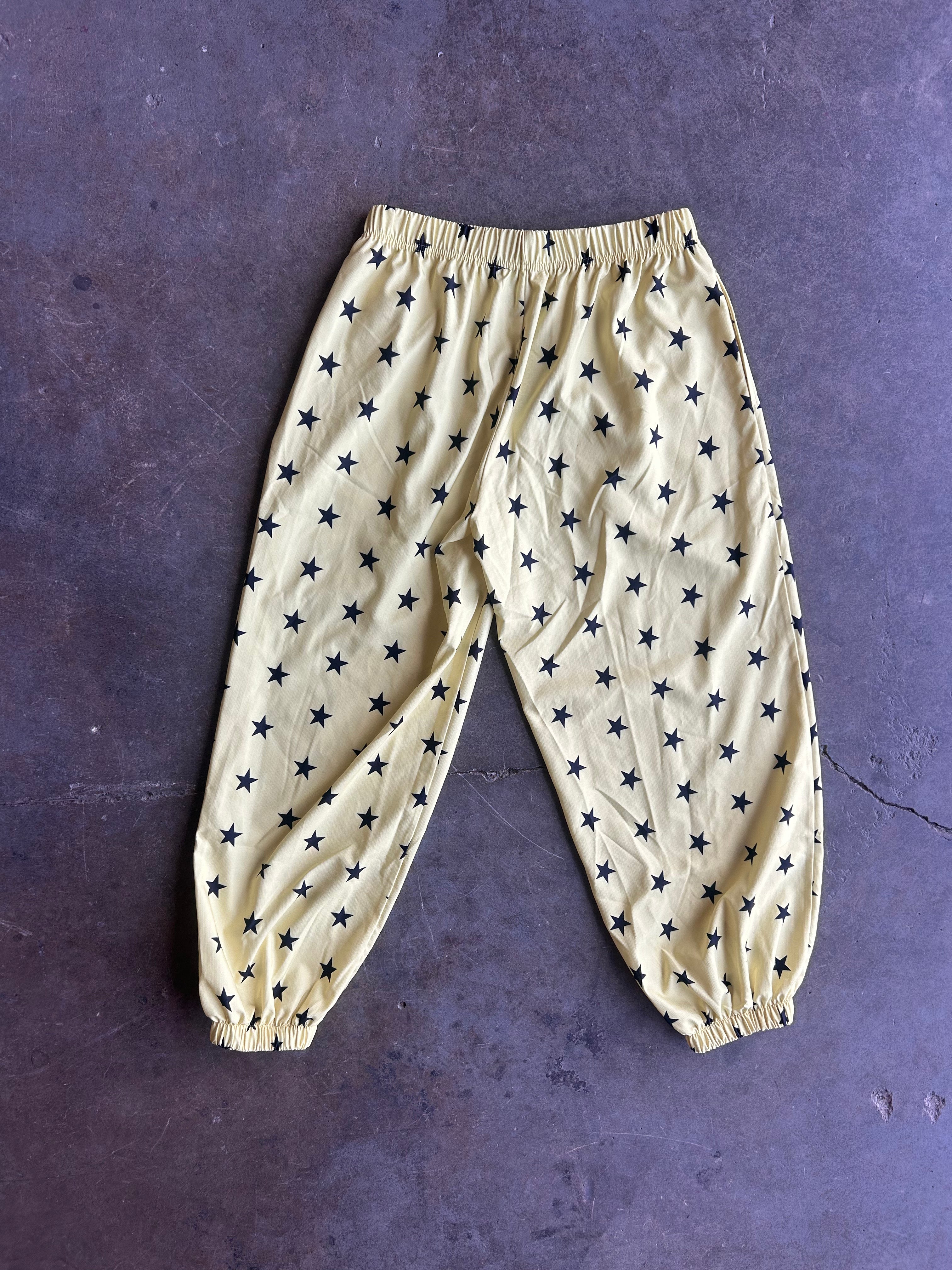 A pair of beige or cream-colored pants with an all-over navy blue star pattern, laid flat on a dark textured surface