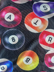 A close-up of a dark fabric printed with colorful billiard balls featuring letters A, S, T, R, B, and 8