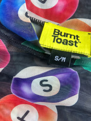 Close-up of a garment tag reading 'Burnt Toast' and 'S/M' on a dark mesh fabric with a colorful pool-ball print