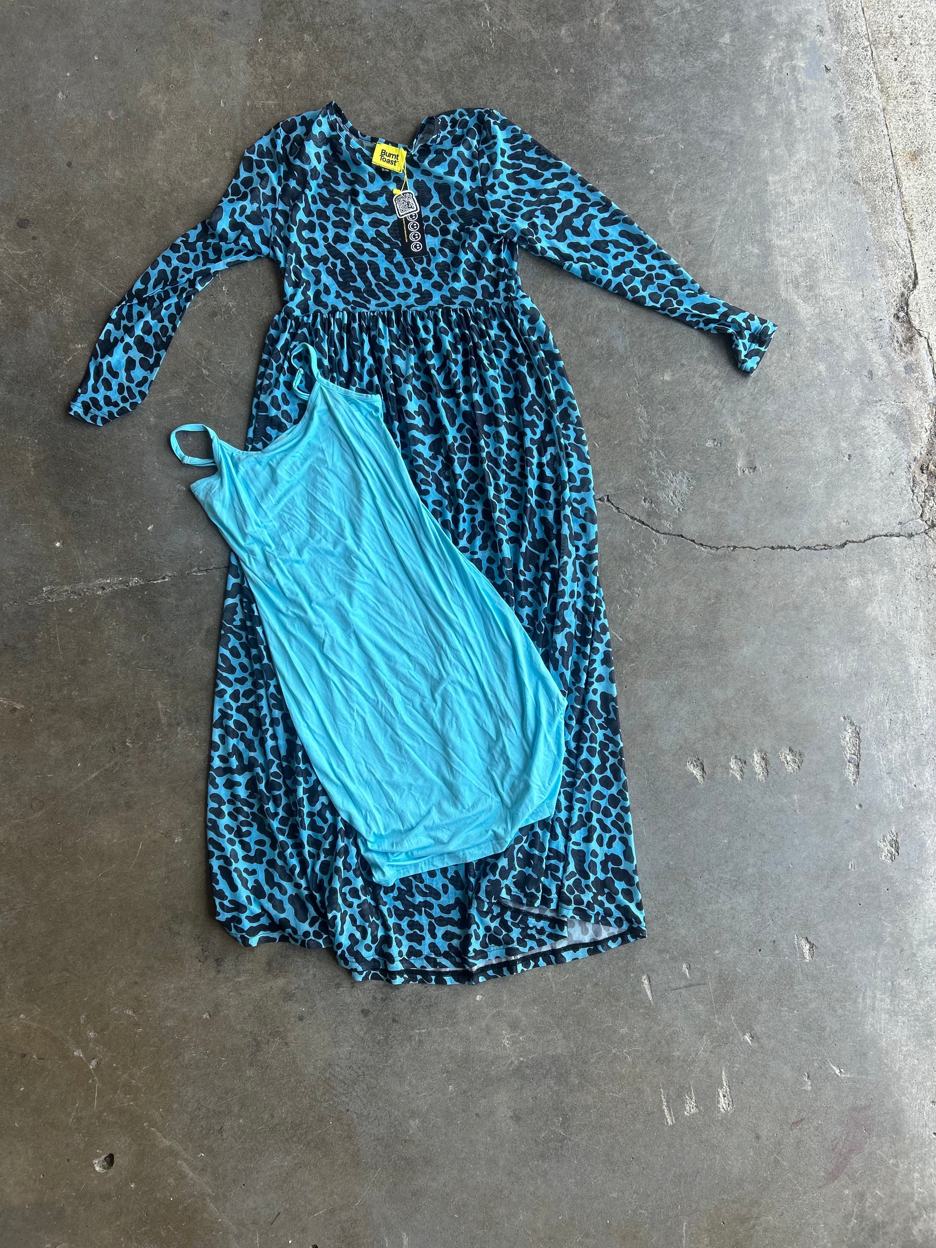 A long-sleeve blue and black leopard print dress with a turquoise slip-on tank top laid flat on a concrete floor
