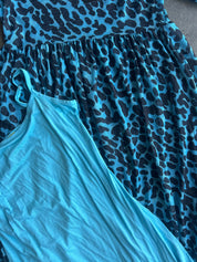 A close-up of a blue and black leopard print dress layered over a solid light blue sleeveless top, laid flat on a neutral gray surface