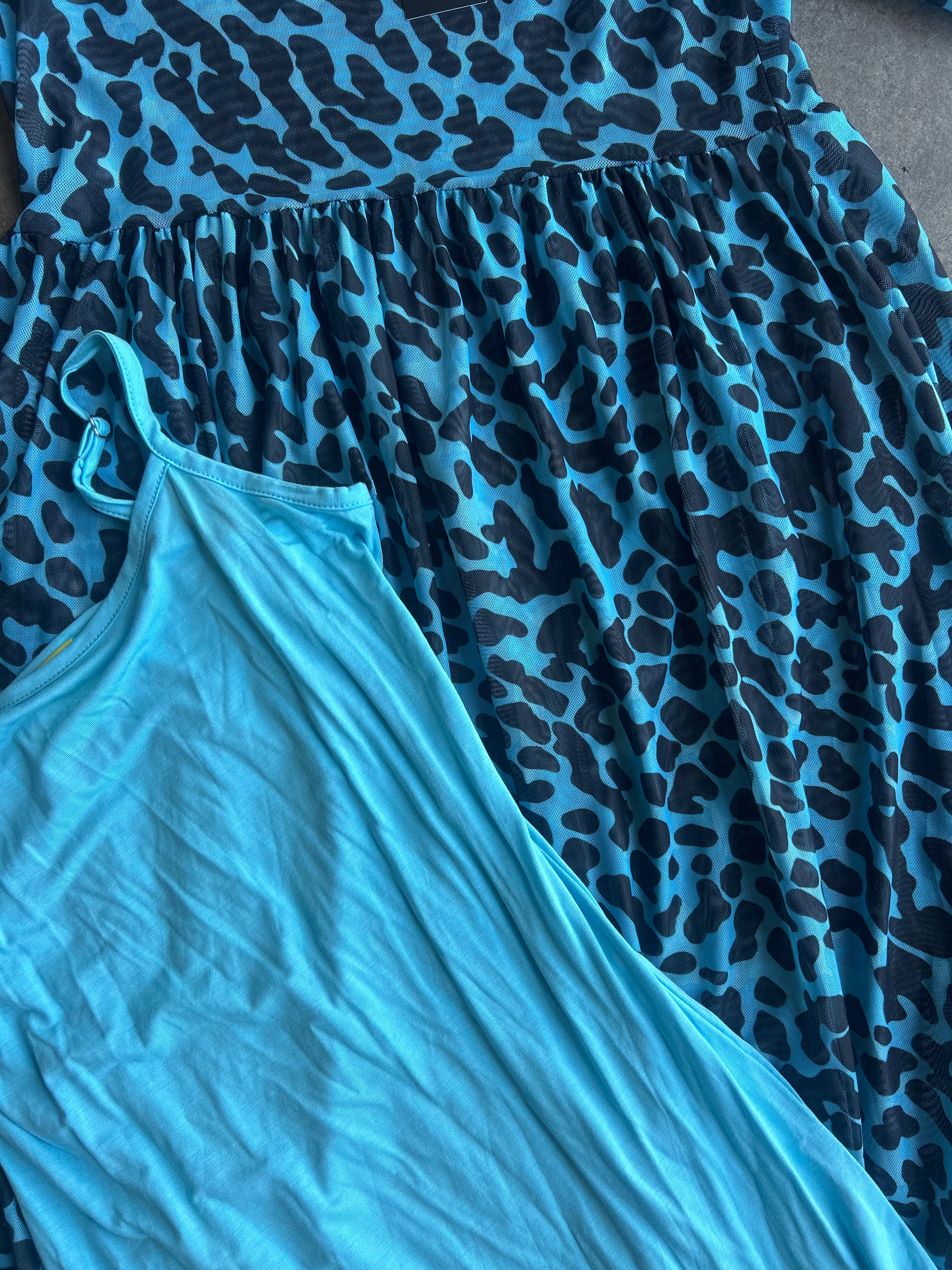 A close-up of a blue and black leopard print dress layered over a solid light blue sleeveless top, laid flat on a neutral gray surface
