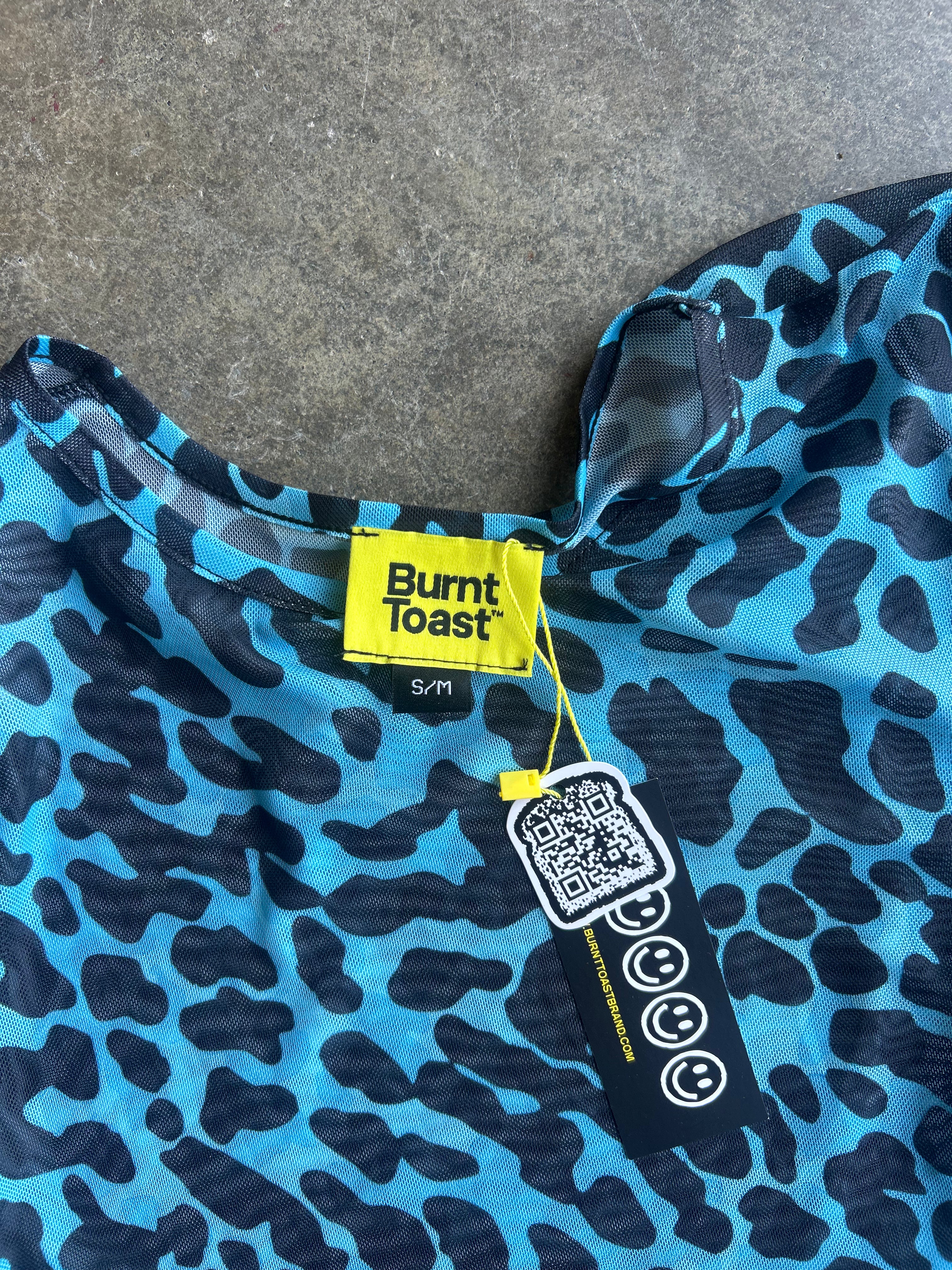 Close-up of a blue and black leopard print garment with a visible Burnt Toast brand label and hangtag on a gray concrete surface