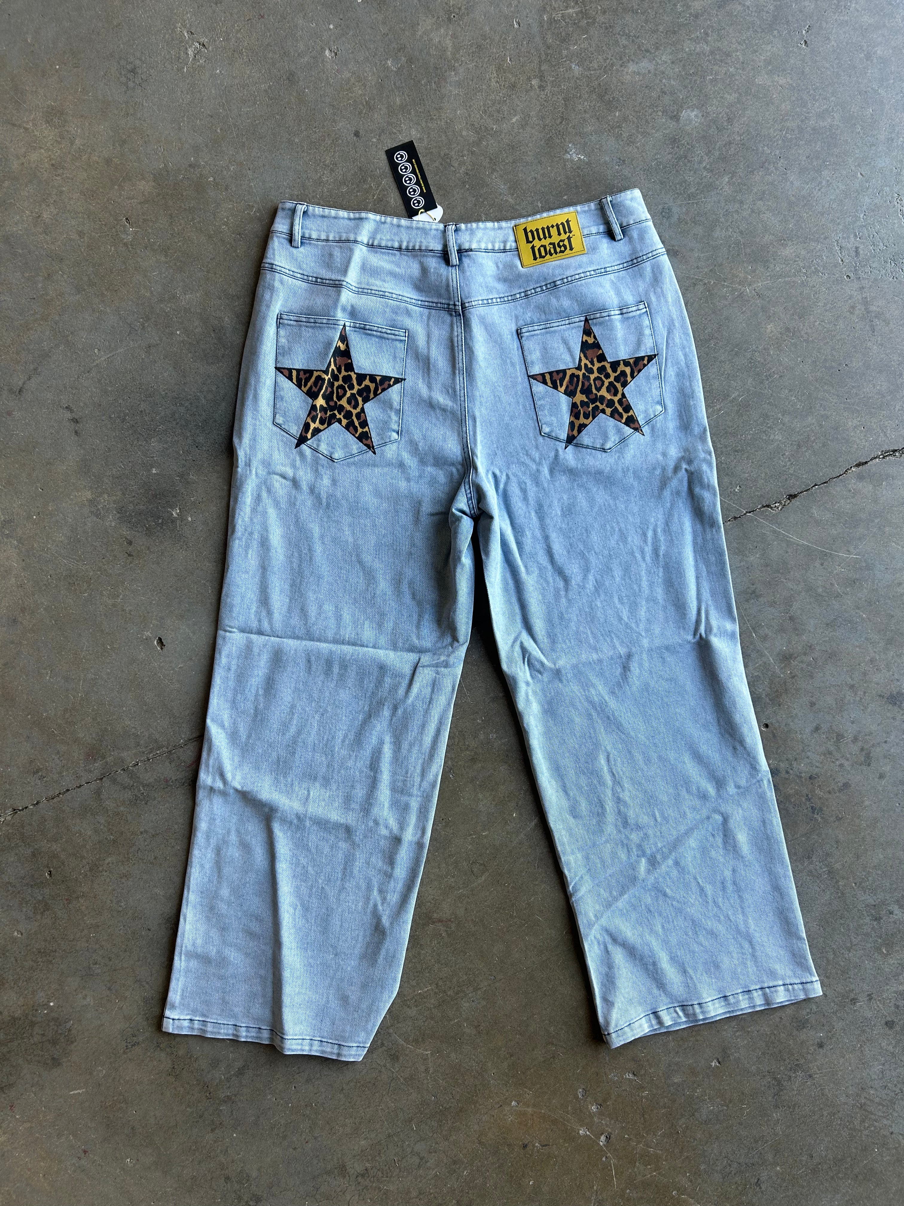 Light wash denim cropped jeans with star-shaped leopard-print patch back pockets, laid flat on a concrete floor