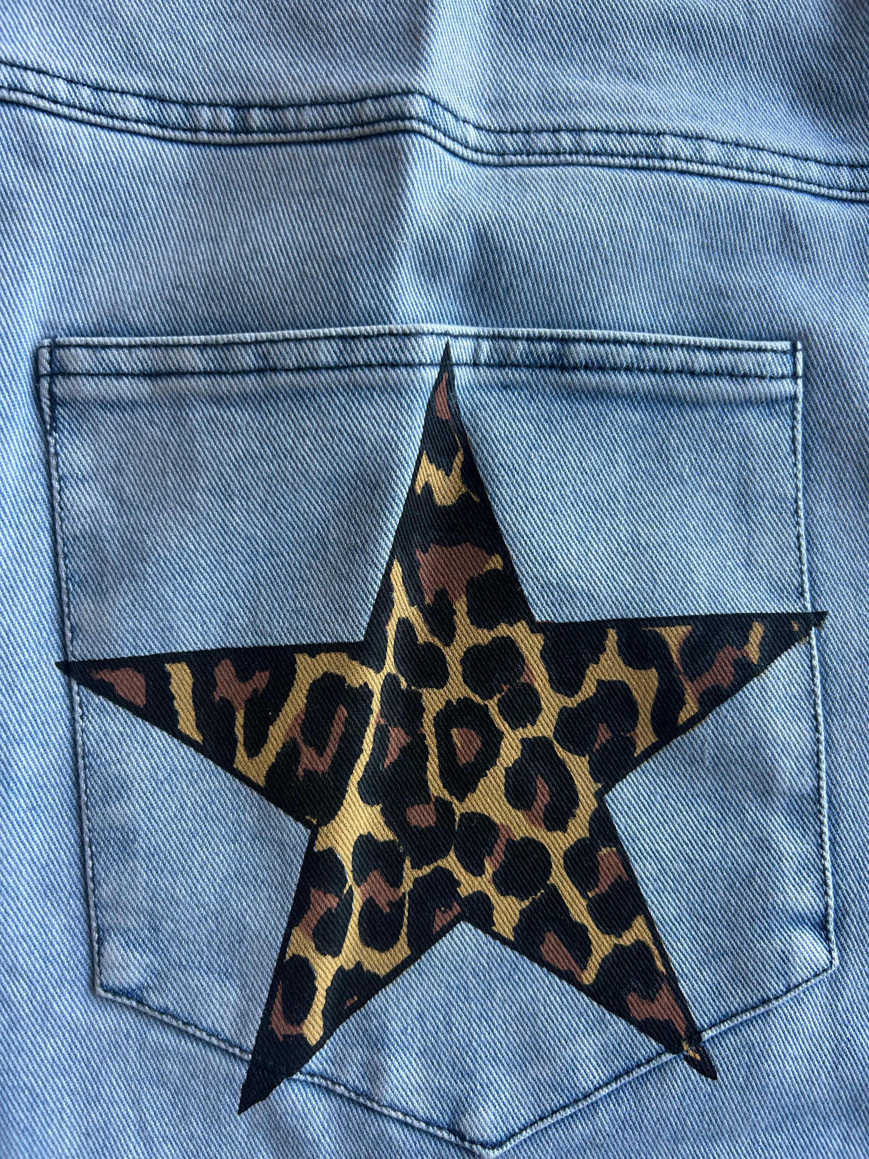 Close-up of the back pocket of a light blue denim jacket, featuring a large star patch with a leopard print pattern in black, brown, and tan