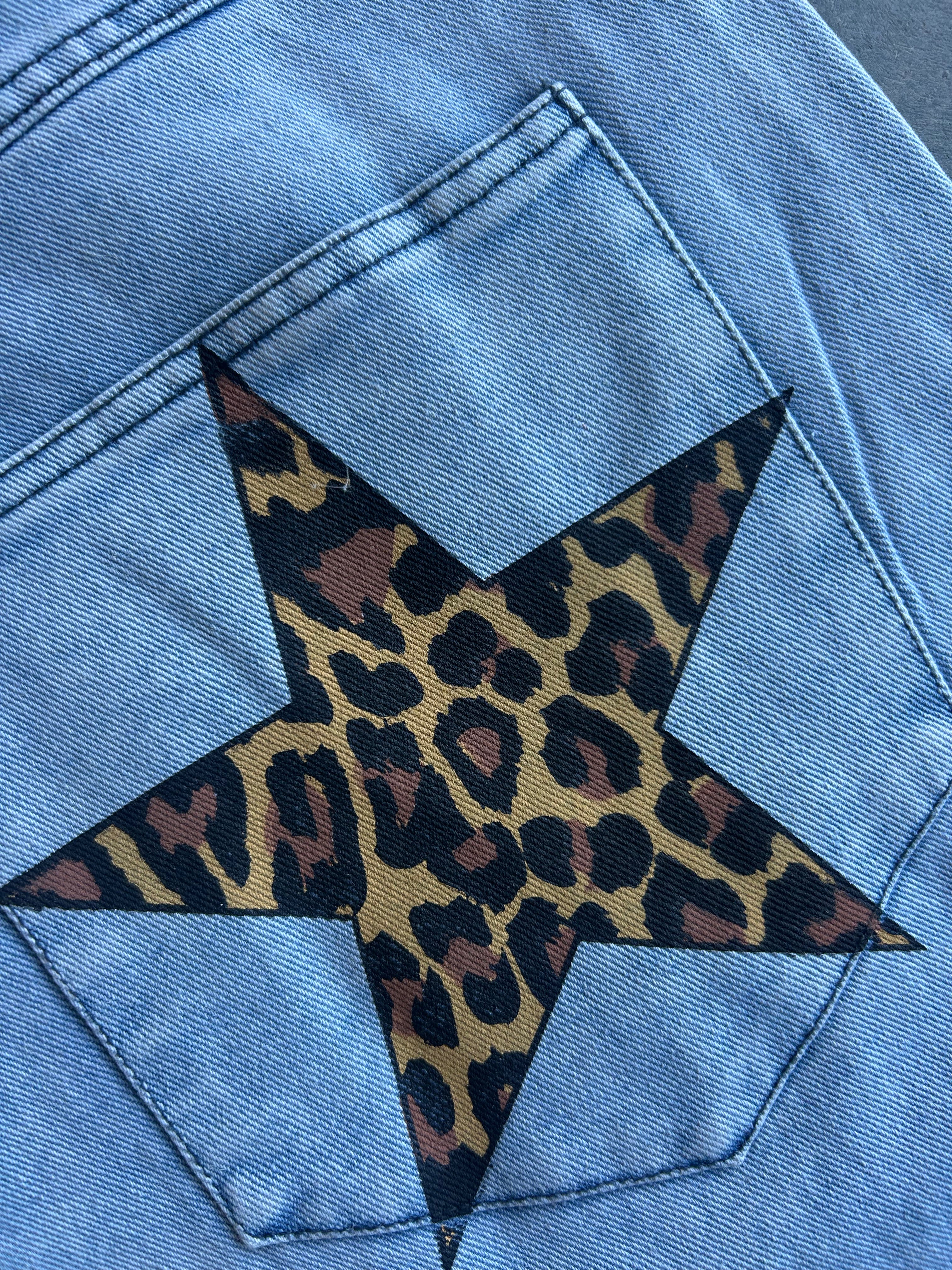 Close-up of a light blue denim jacket showing a large star-shaped leopard print patch applied to the back pocket