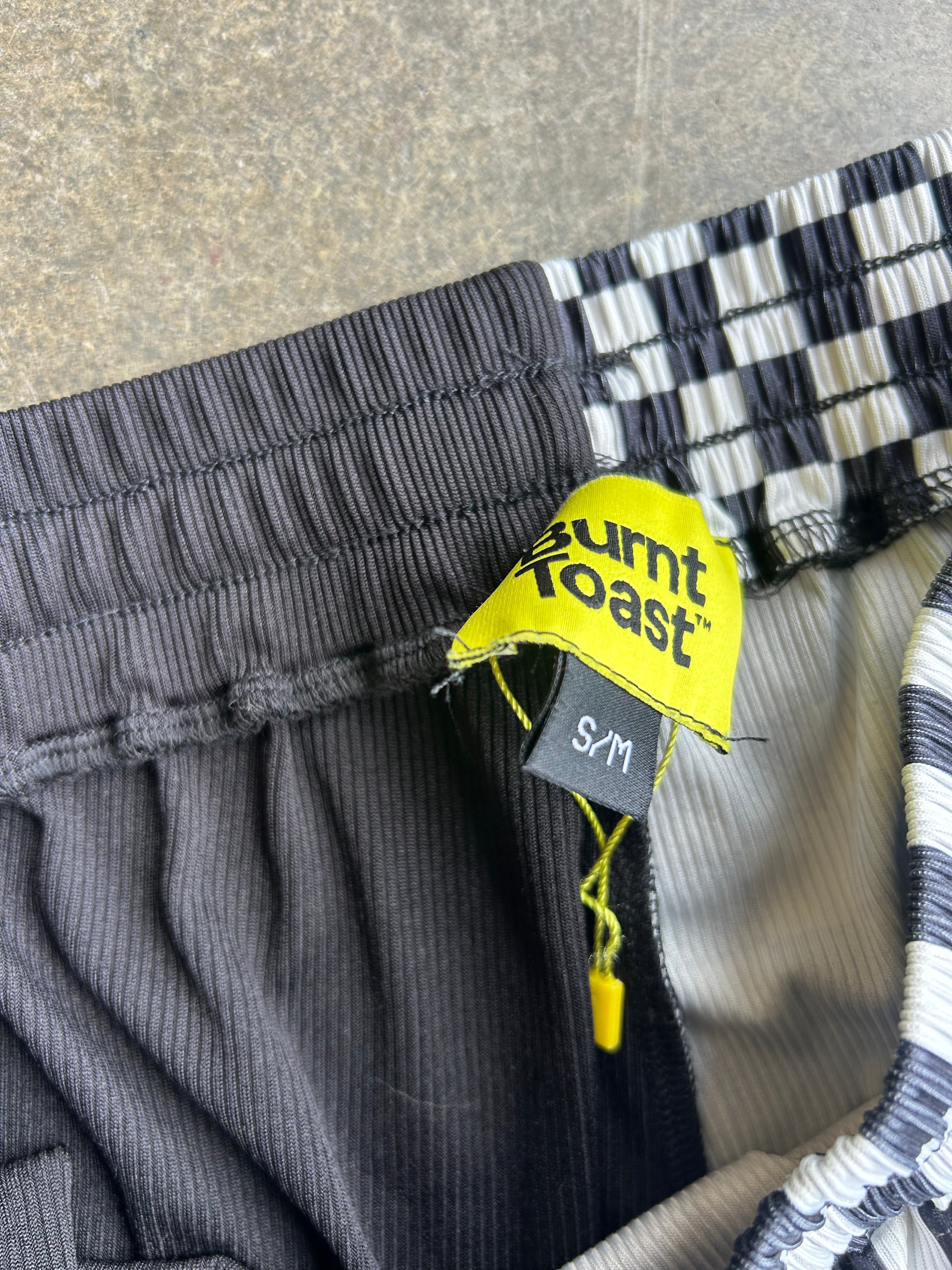 Close-up of a pair of charcoal gray ribbed shorts with a black and white checkered pattern on the waistband and a yellow Burnt Toast size tag