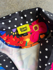 Close-up of a Burnt Toast garment laid flat on a stone surface, showing a black fabric with white polka dots and a colorful floral lining with a bright yellow brand label