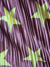 A close-up of pleated fabric with a purple base and large lime green star patterns.