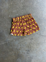 A pair of brown shorts with a yellow star pattern, laid flat on a gray concrete floor