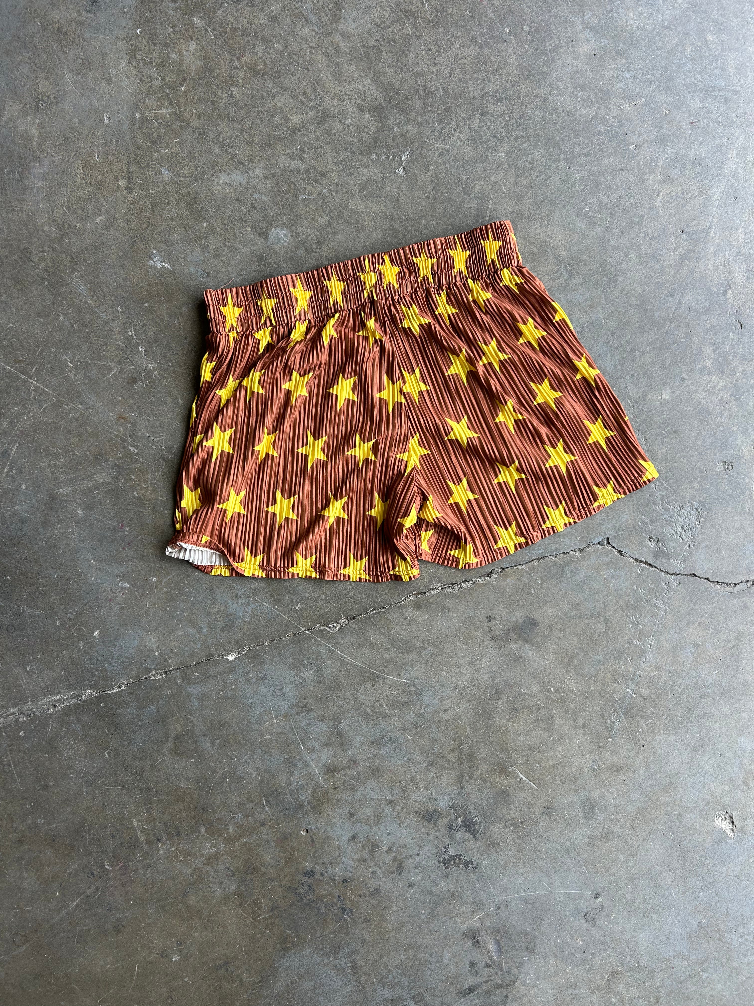 A pair of brown shorts with a yellow star pattern, laid flat on a gray concrete floor