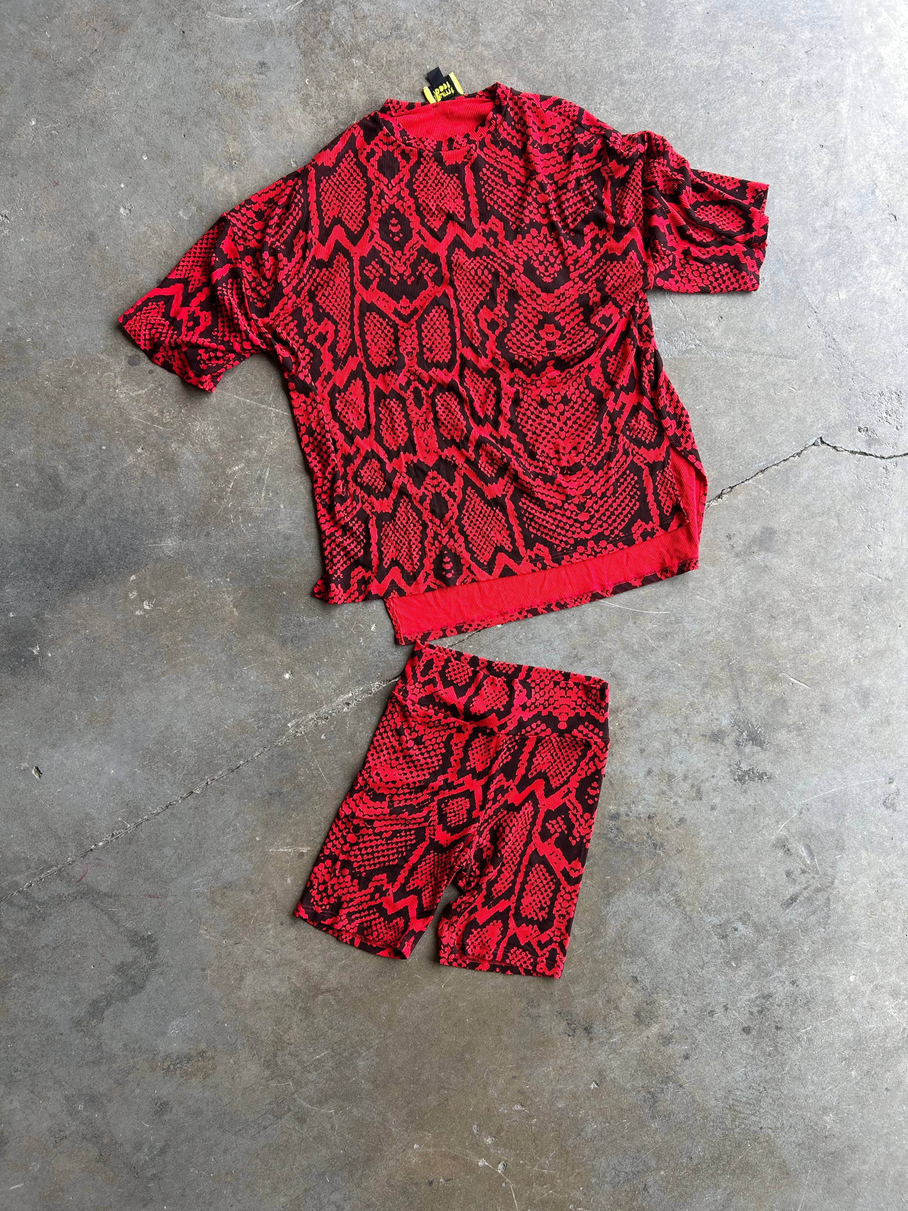 A red and black snakeskin-patterned short-sleeve top and matching shorts laid flat on a gray concrete floor