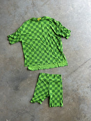A green checkerboard short-sleeve shirt and matching shorts laid flat on a gray concrete floor