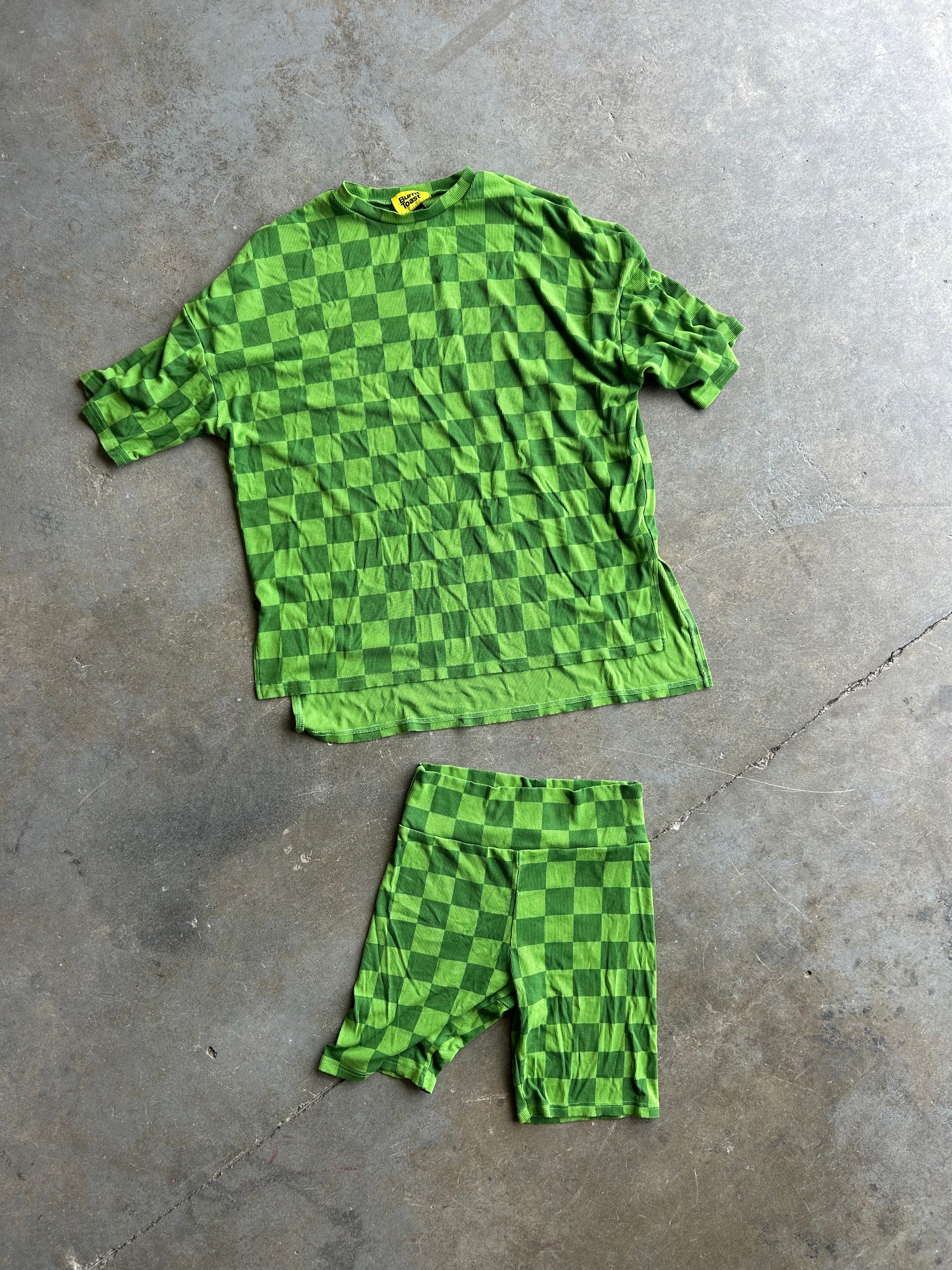 A green checkerboard short-sleeve shirt and matching shorts laid flat on a gray concrete floor