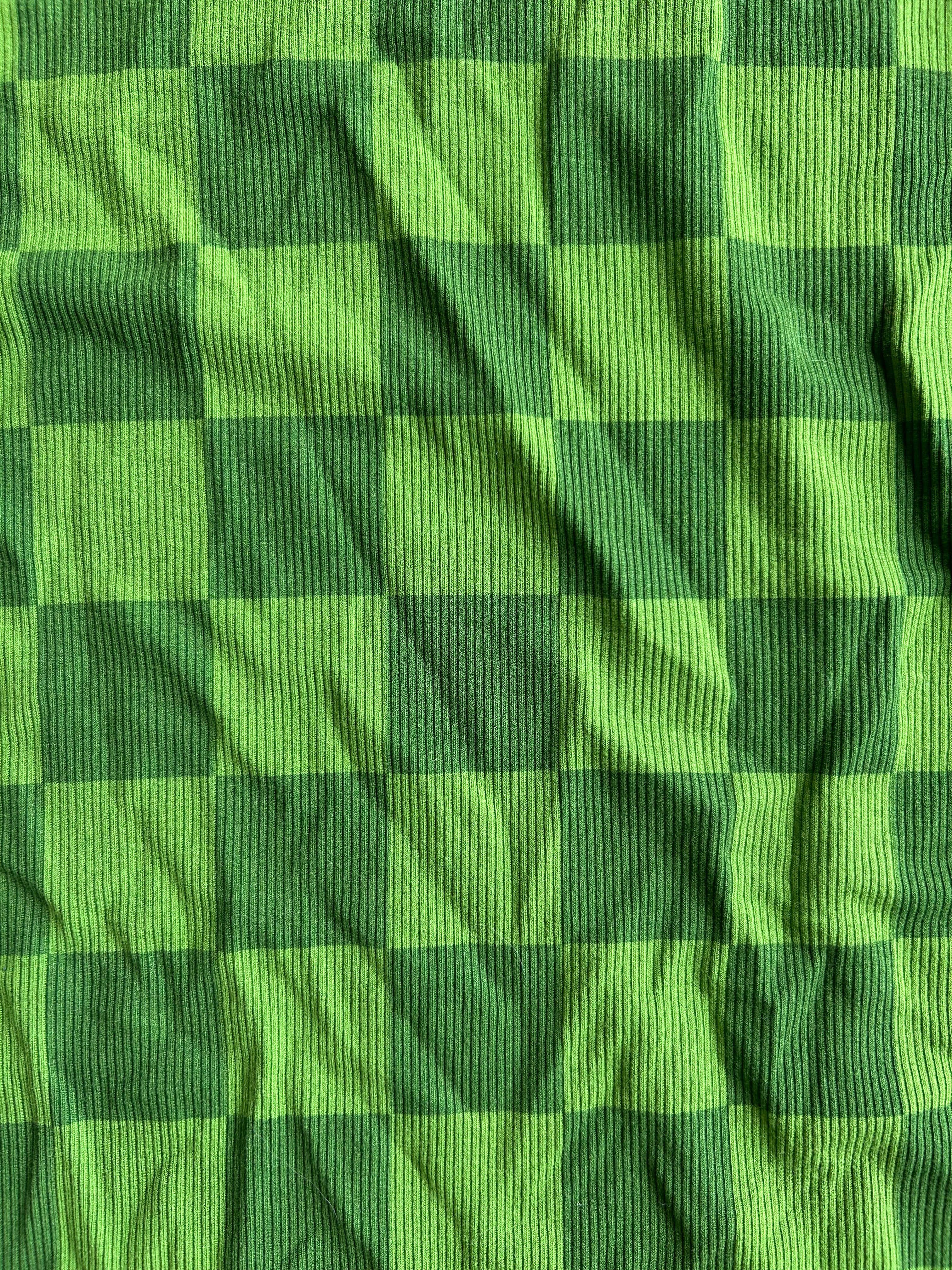A close-up of a green and dark green checkered fabric with a ribbed texture, showing the pattern and material details
