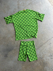 A green and dark green checkerboard short-sleeve t-shirt and matching shorts laid flat on a gray concrete floor