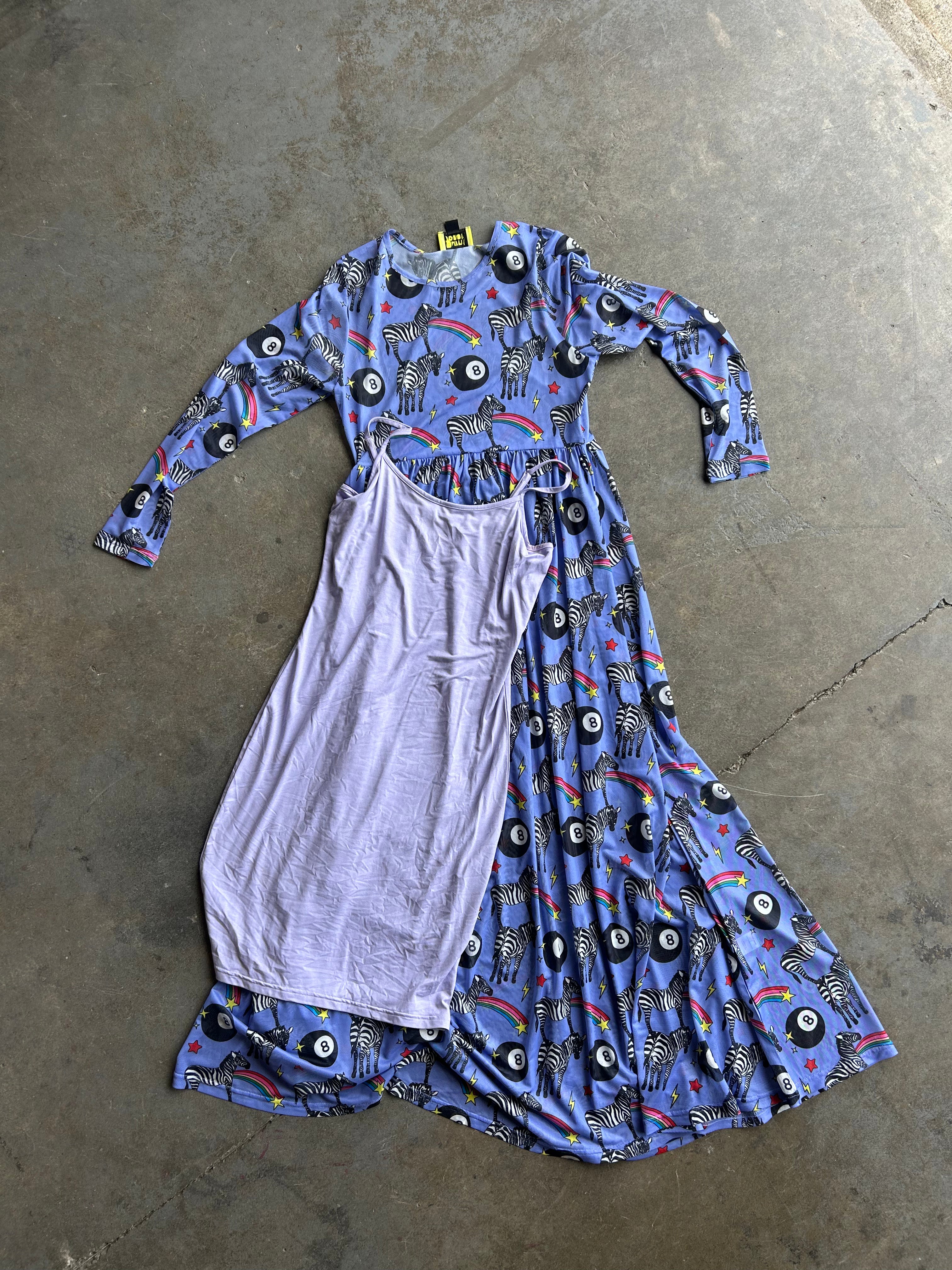A long-sleeve dress laid flat on a concrete floor, featuring a blue base with a black, white, and multicolor zebra-and-eye print on one side, and a solid light lavender panel on the other
