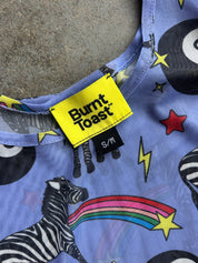 Close-up of a Burnt Toast garment with a bright yellow brand label and a colorful zebra-and-rainbow print on a light blue-purple background