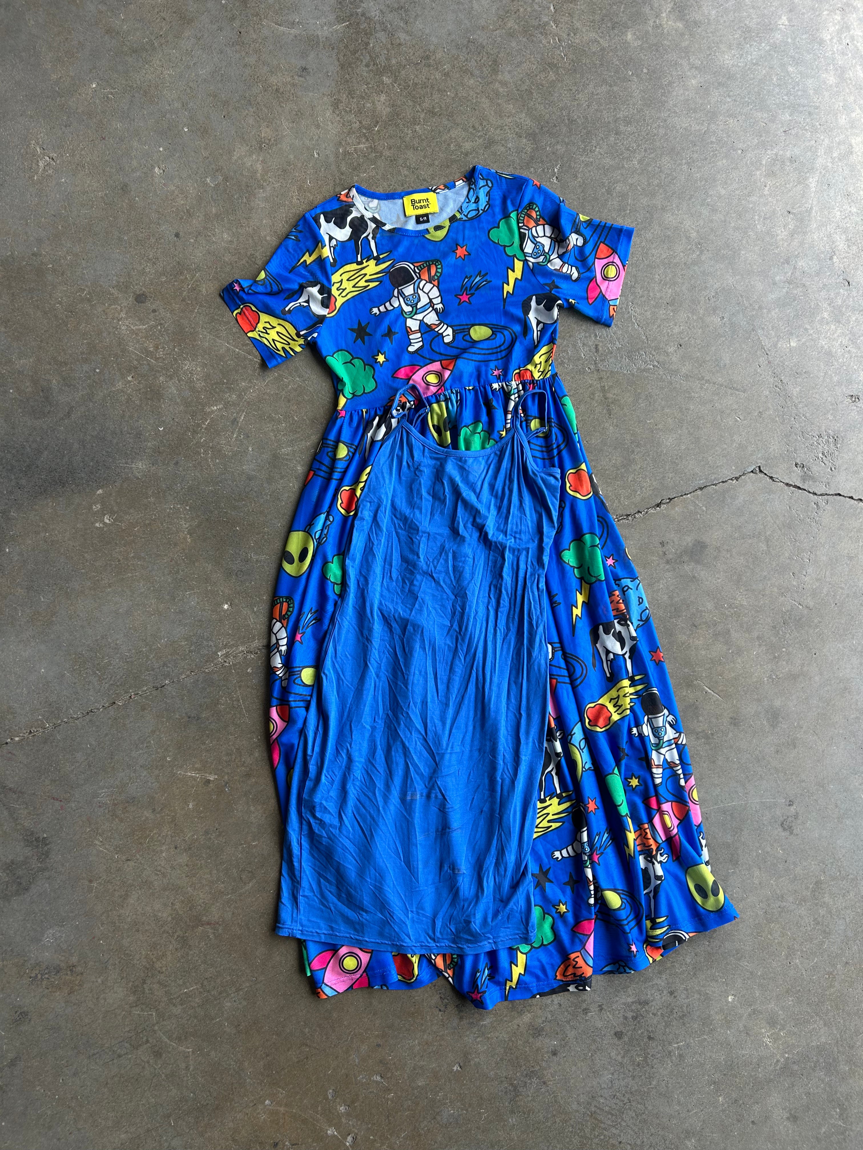 A mesh style blue dress with a colorful space-themed print, laid flat on a gray concrete floor