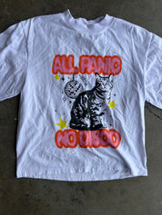 Close up of a white short-sleeve graphic t-shirt laid flat on a concrete floor. The shirt features a black cat illustration with red bubble text reading 'ALL PANIC NO DISCO' and small yellow stars