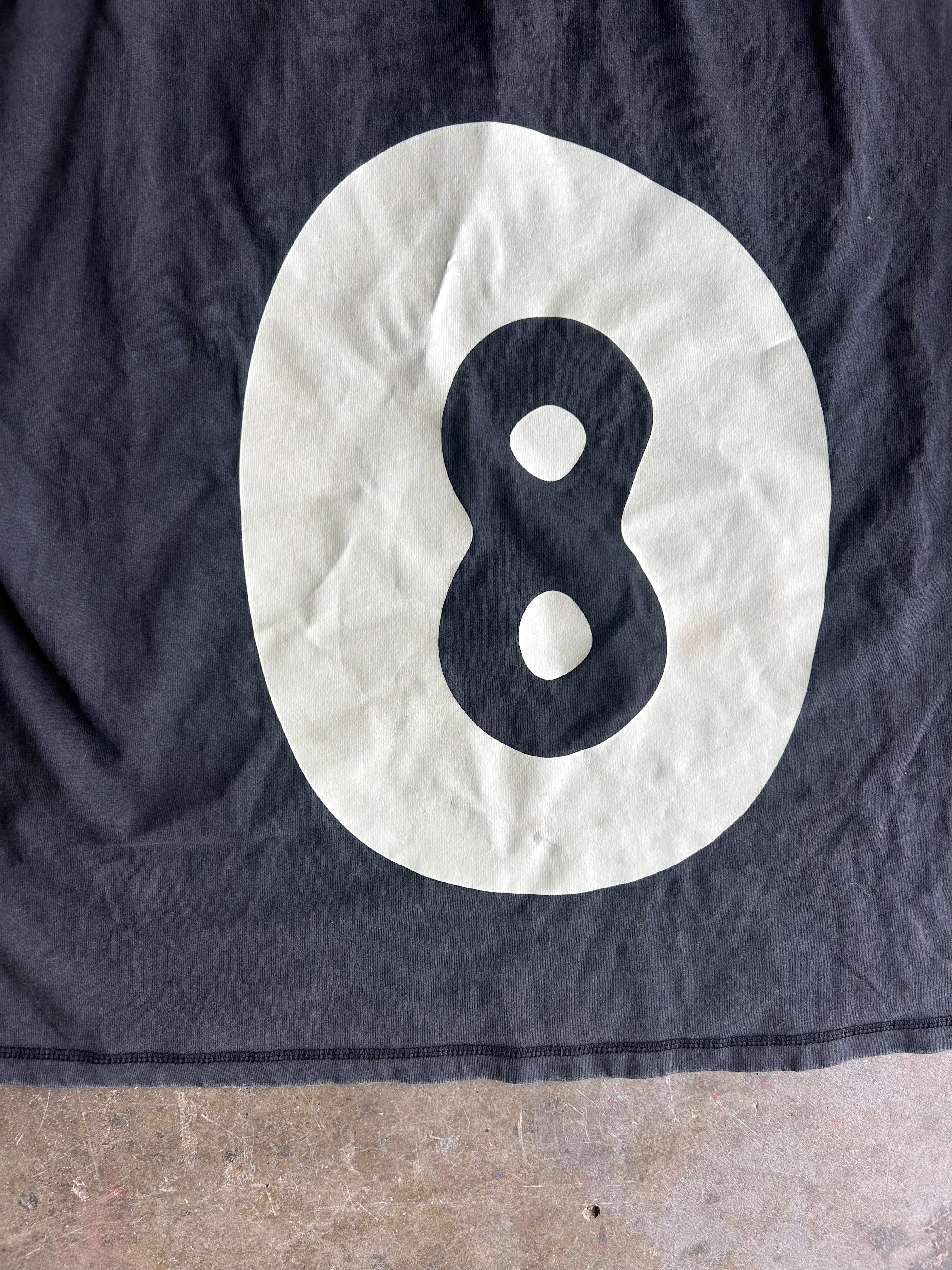 A close-up of a dark black fabric shirt, featuring a large cream-colored oval with a black number 8 printed inside it