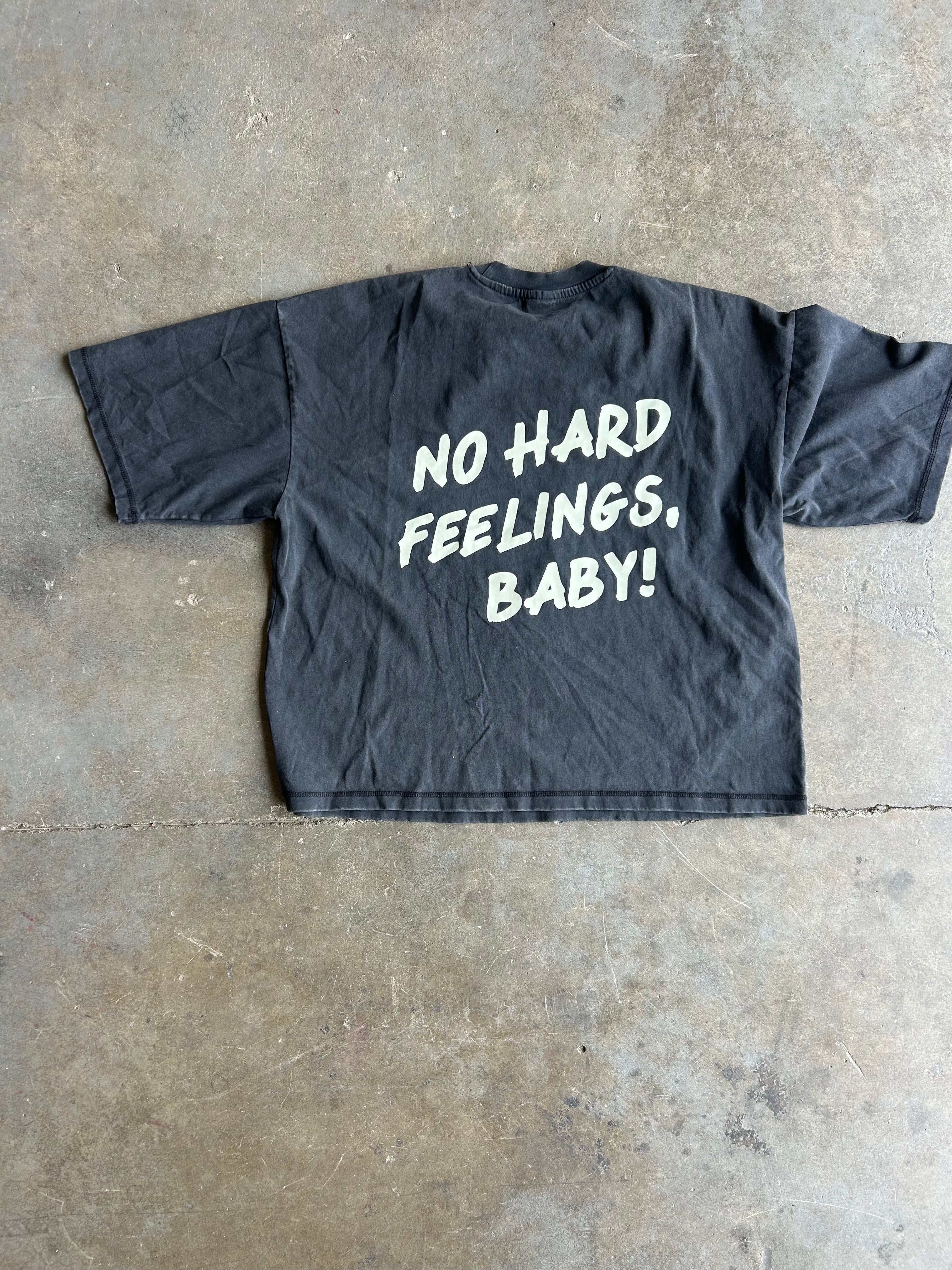 Back of a black graphic tee with the text 'NO HARD FEELINGS, BABY! ' flat lay view on concrete floor 