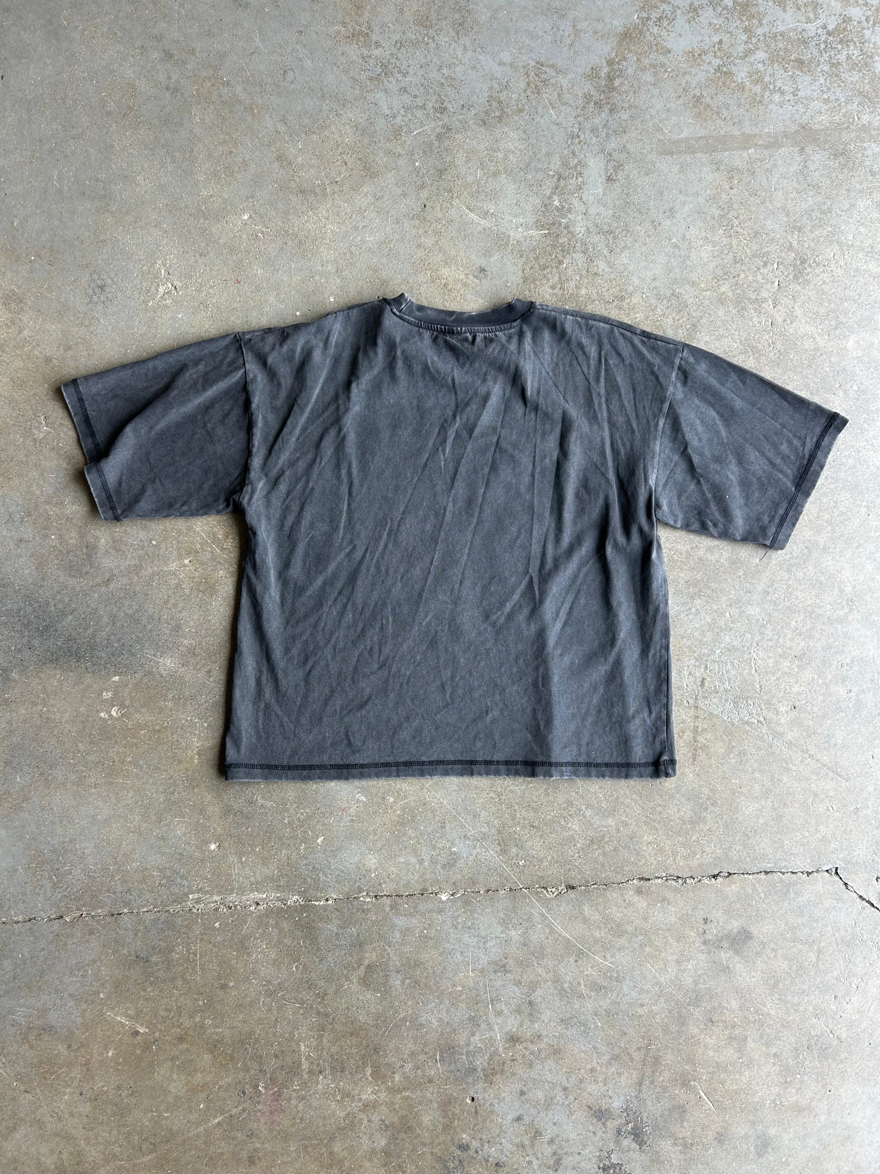 A dark gray washed cotton t-shirt laid flat on a textured concrete floor