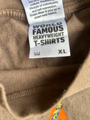 Close-up of a brown T-shirt neck label reading 'WORLD FAMOUS HEAVYWEIGHT T-ShIRTS' with size 'XL' and a partial orange graphic on the shirt