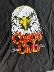 A close-up of a black graphic t-shirt featuring a bald eagle illustration and the words 'Chaos Club' in red with yellow outlines, along with 'Burnt Toast' in white script.
