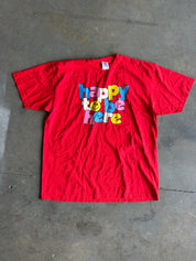 Red graphic tee with Happy to Be Here text on a concrete surface
