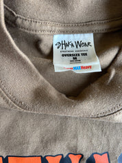 Close-up of the inside collar of a taupe-brown oversized t-shirt, showing the white 'SHIWA WEAR' brand label.